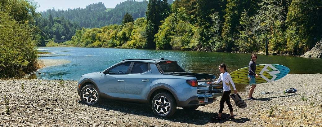 A 2022 Hyundai Santa Cruz parked at the edge of an alpine lake, with people taking paddle boards out of it.