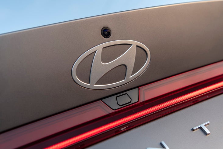 A Hyundai service technician in a navy and grey uniform uses a pneumatic impact wrench to secure a car tire in a professional garage.