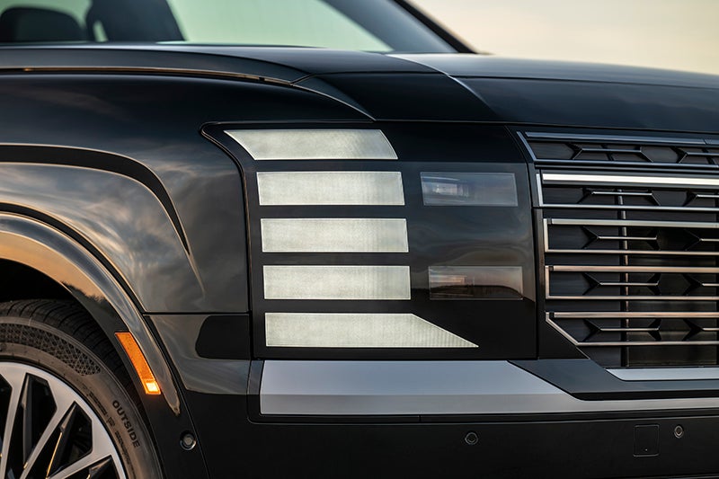 A Hyundai service technician in a navy and grey uniform uses a pneumatic impact wrench on a car tire in a professional garage.