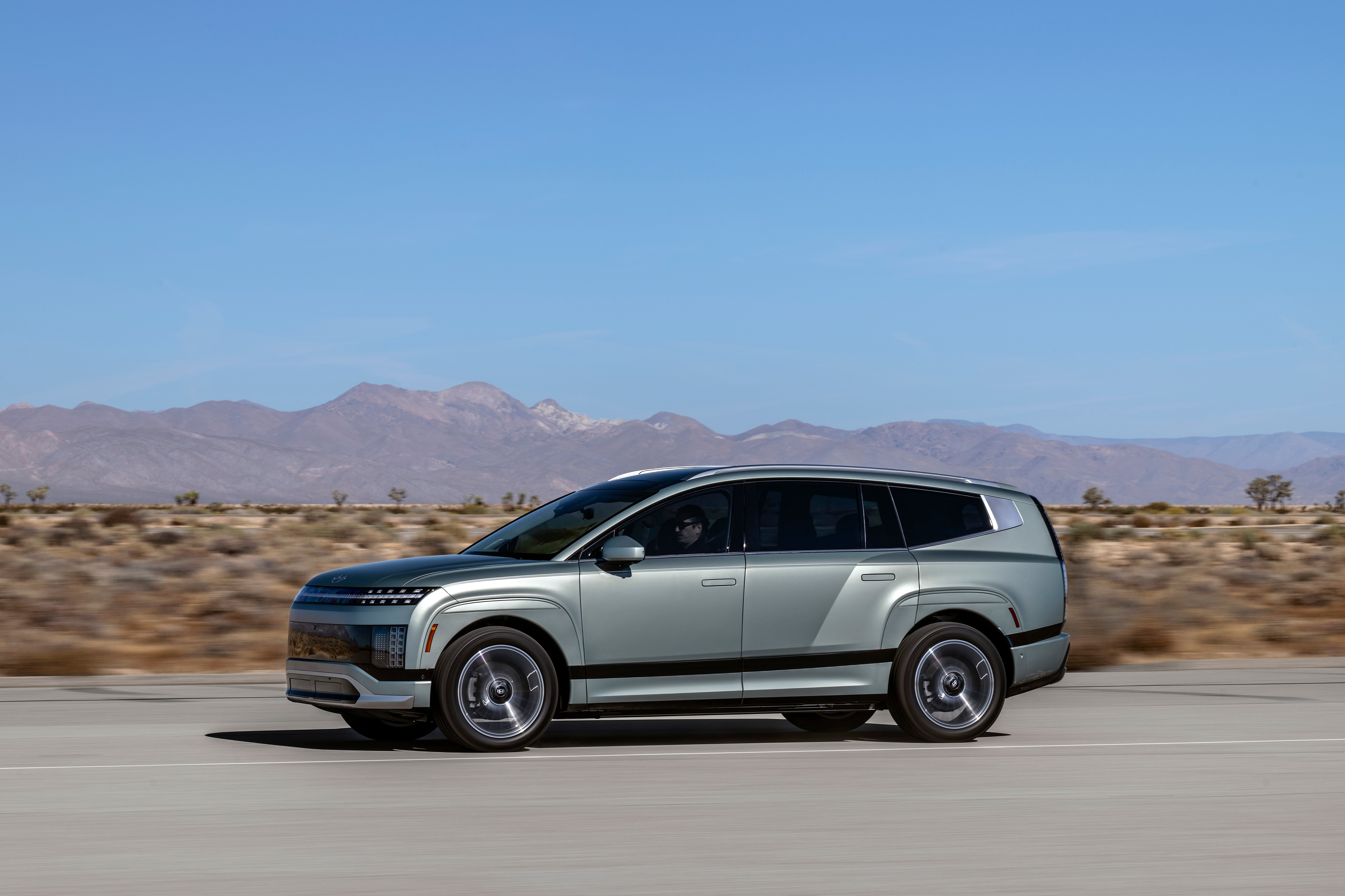 A silver 2026 Hyundai Ioniq 9 in Avondale drives to the left on a two-lane highway through the Arizona desert with arid mountains in the background.